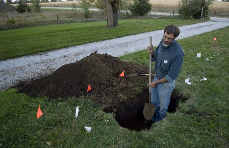 Homeowner digging a hole in a yard marked with utility flags