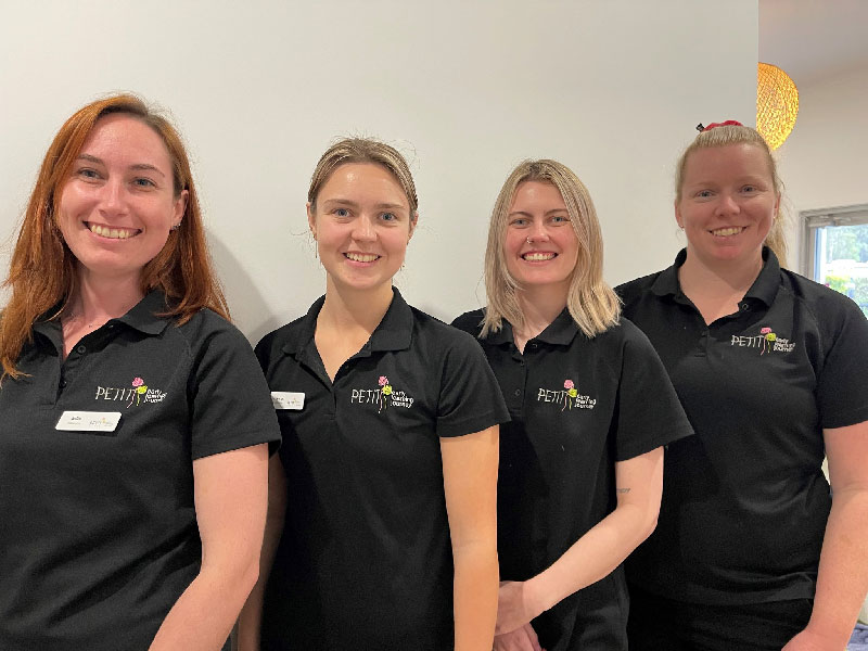 Four lead educators, also known as room educators, wearing black uniform shirts and name badges with Petit Early Learning Journey's logo on it stand facing the camera and smiling as they look forward to new initiatives to come from the employee engagement survey.