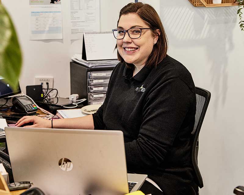 A Petit ELJ educator who is part of the centre's leadership team, sits at a table with a laptop and PC as she checks documentation, a key component of the NQS.