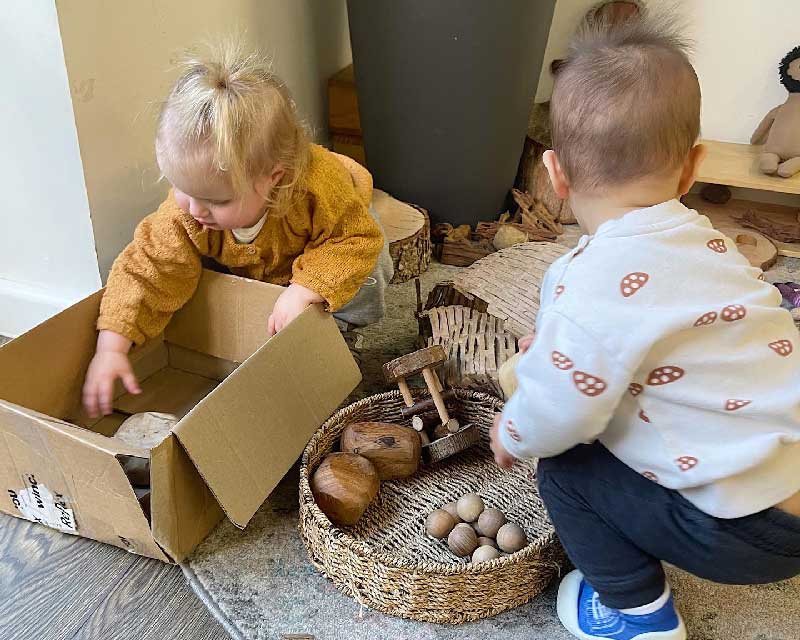  Two children sort through containers and cardboard boxes for loose parts group play game ideas.