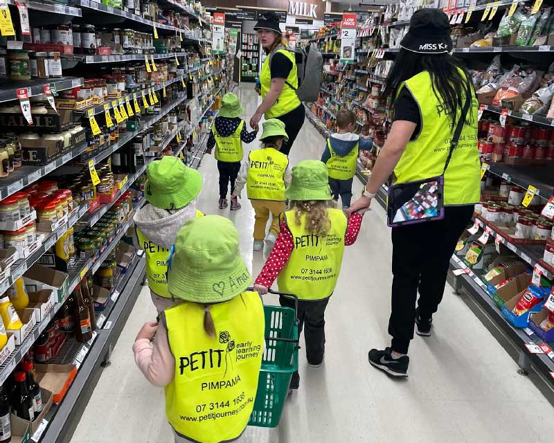 Children from Petit ELJ walk down a grocery isle with educators learning about how to budget and save money.