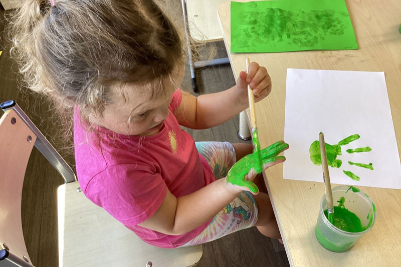 A child paints their hands green to make handprints and record the size of their hand. Record keeping is one of the benefits of a baby or older child keepsake box.