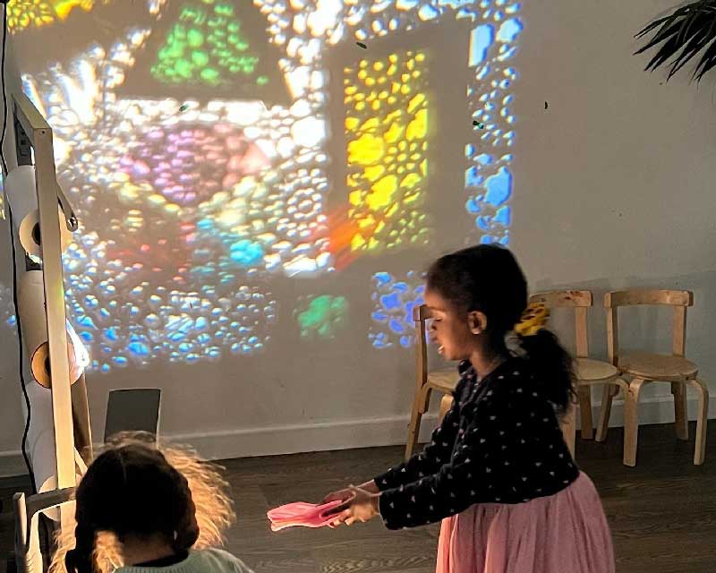 Two children engage in shadow and light play using a projector.
