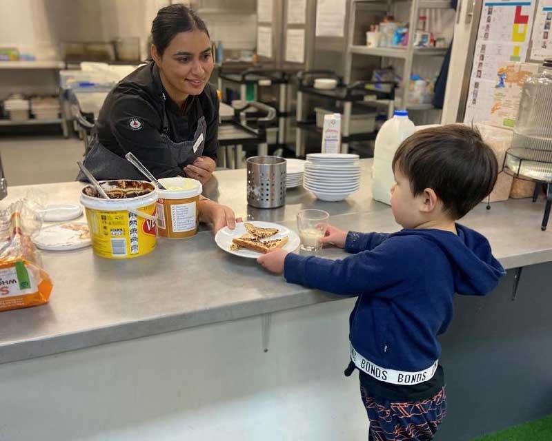 Chef Sandeep at Petit Forest Hill passes a child a vegemite sandwich.