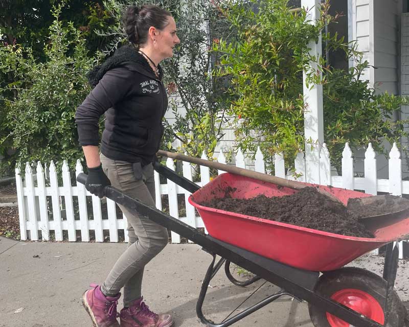 A Petit ELJ chef moves a wheelbarrow filled with dirt for a garden bed.