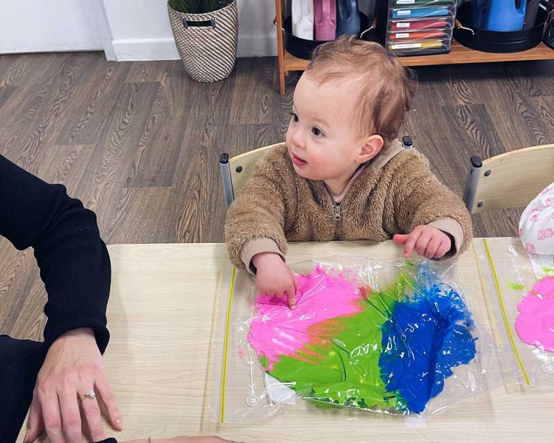 A young child with a clip-lock bag of regular gooey slime in three shades, learns how to squish and poke with their fingers.