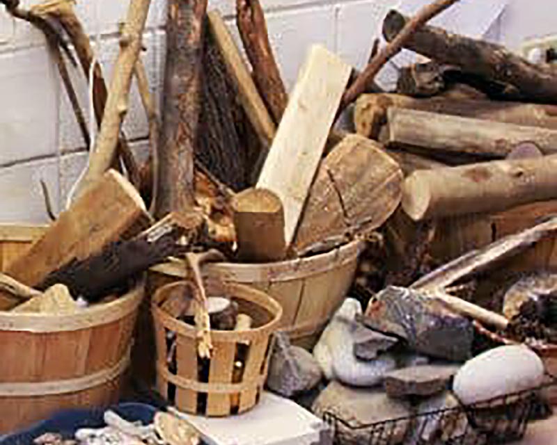 A pile of natural loose parts play including branches, wooden planks and stones of different sizes.