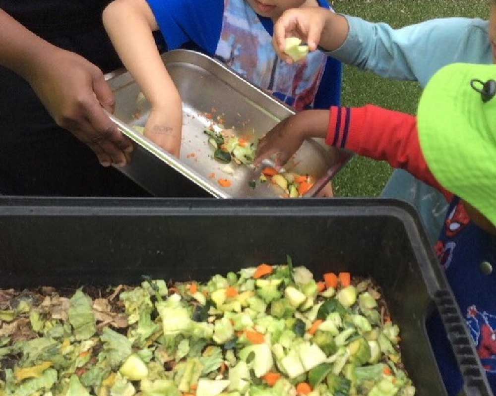 Children use their hands to grab up leftovers in a silver tray from the kitchen to feed and look after the worms' well-being.