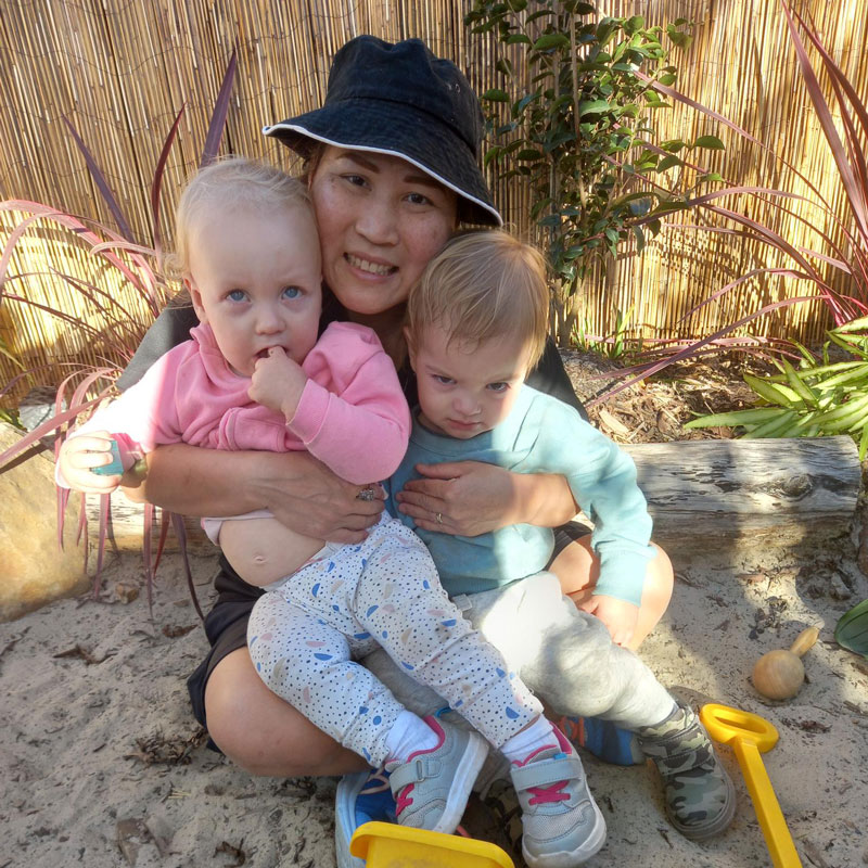 Apple, our exceptional team member for June holds two children while sitting surrounded by plants and sand.