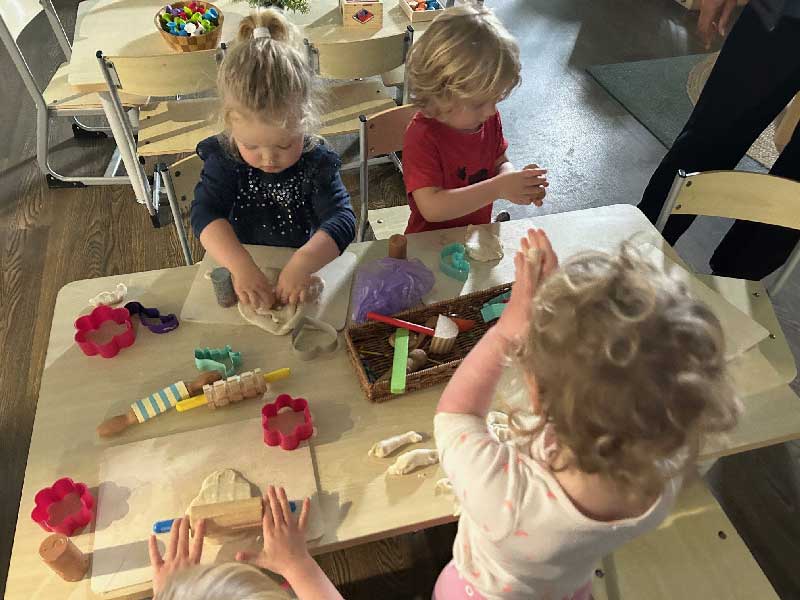 Children building close secure relationships at Petit ELJ. Four children stand around a table rolling dough and making shapes.