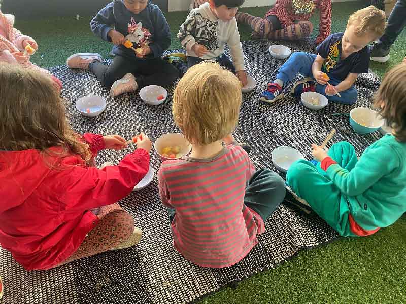 A group of children from Petit ELJ sit on a mat for an outdoor picnic where they are encouraged to regulate their emotions.