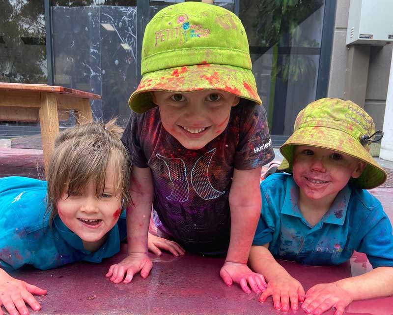 Three girls out in the rain indulge in play-based learning in preschools for children.