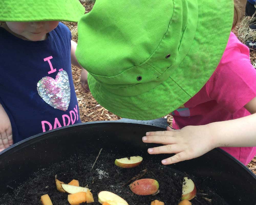 Children peer into the top of an earth worm farm to see how how a worm farm works.