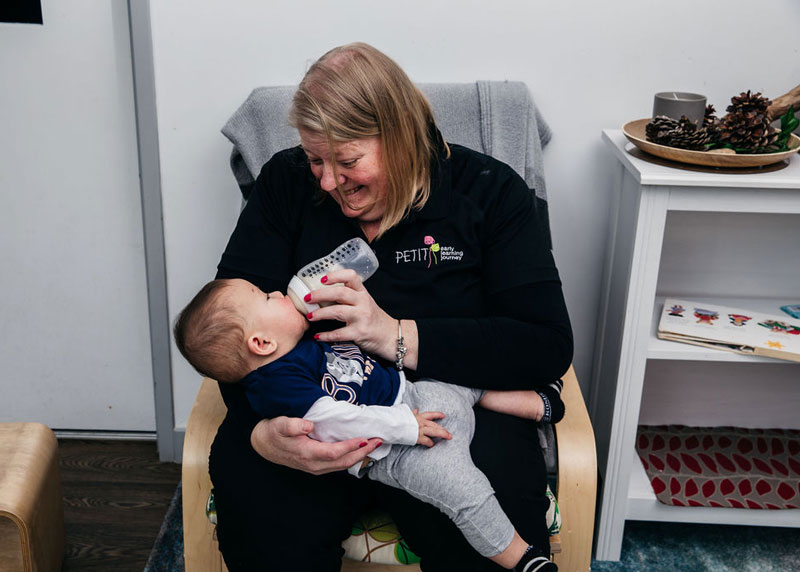 An Educator makes eye contact while holding a child and bottle feeding practising the methods gained from participating in the Circle of Security courses.