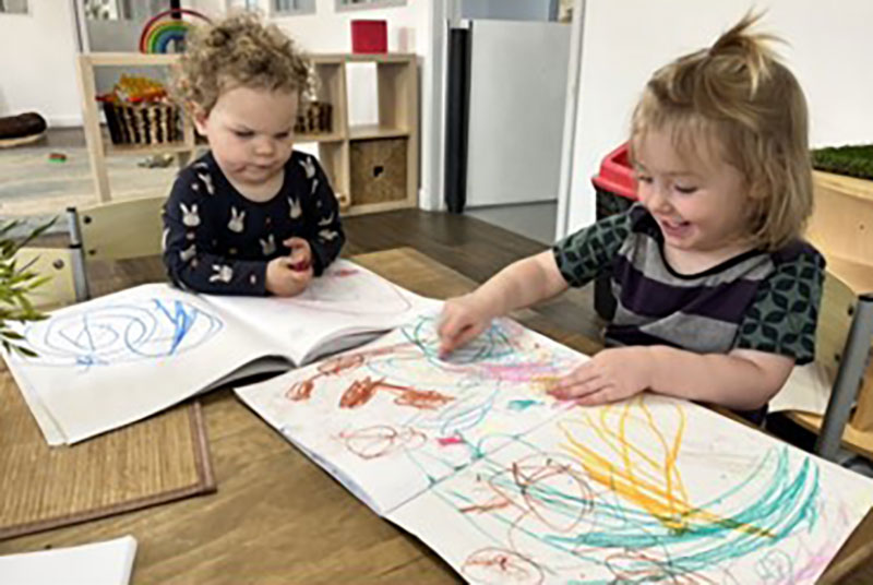 Two children expressing their creativity with crayons and paper at a table.