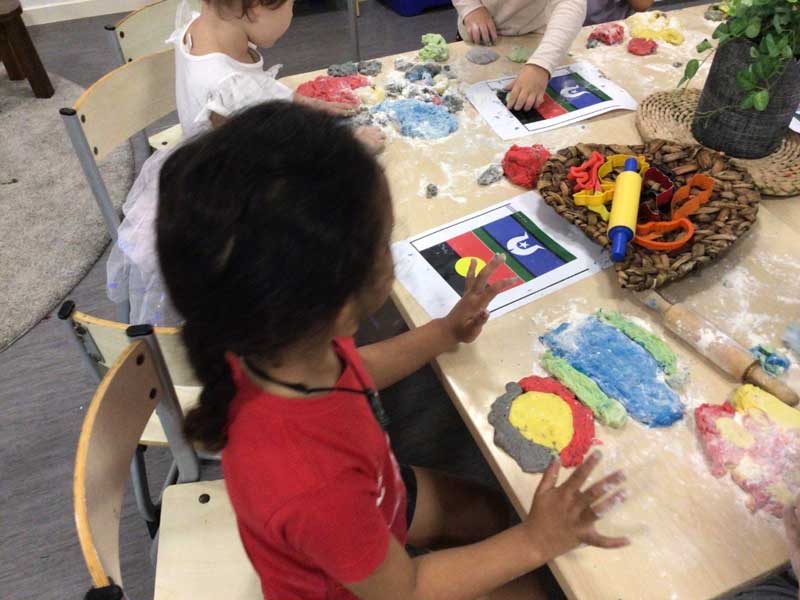  A child sits in a group experience to embed indigenous perspectives at an early childhood service reinterpreting the Aboriginal and Torres Strait Islander flags through playdough.