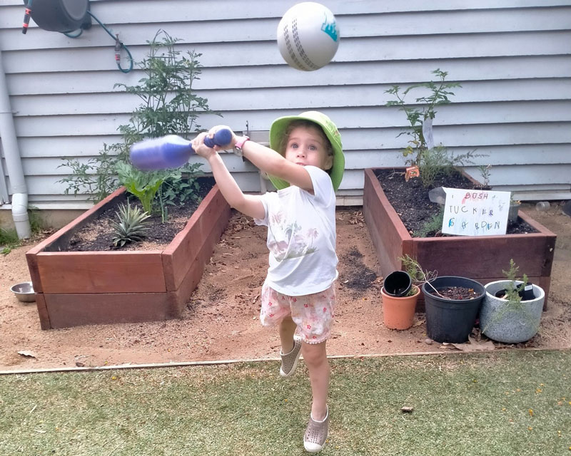 A child swings a bat towards a ball in a sports based extracurricular activity at Petit ELJ Wooloowin.