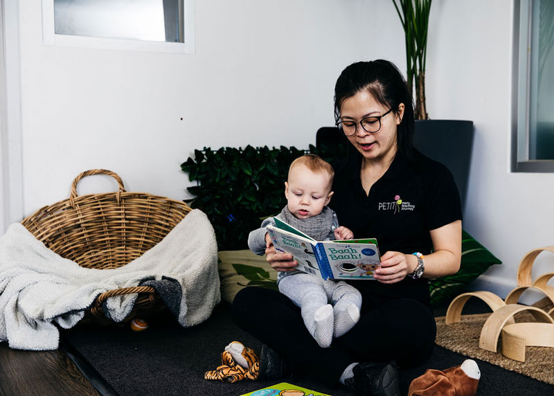 An Educator holds a young infant in her lap while reading and developing their relationship using the Circle of Security roadmap.