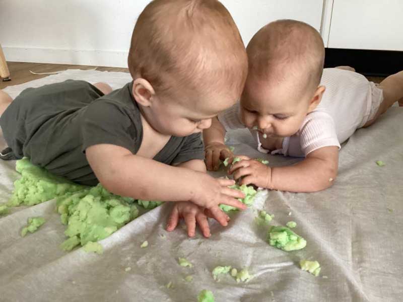 Two babies happily play with edible playdough unaware of cradle cap side effects.
