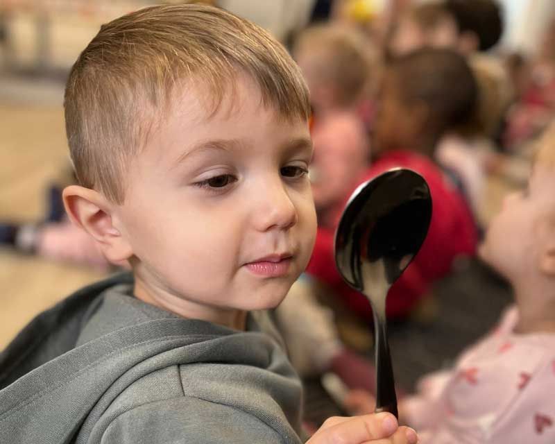 A child looks at his reflection on a spoon while participating in an additional program focused on STEM at Petit ELJ Elderslie.