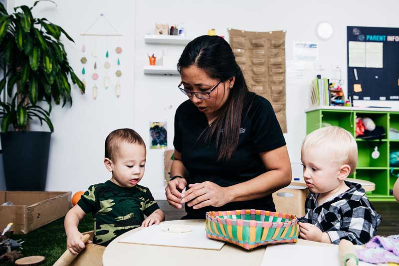 An Educator with two children learning how to use a roller and dough.