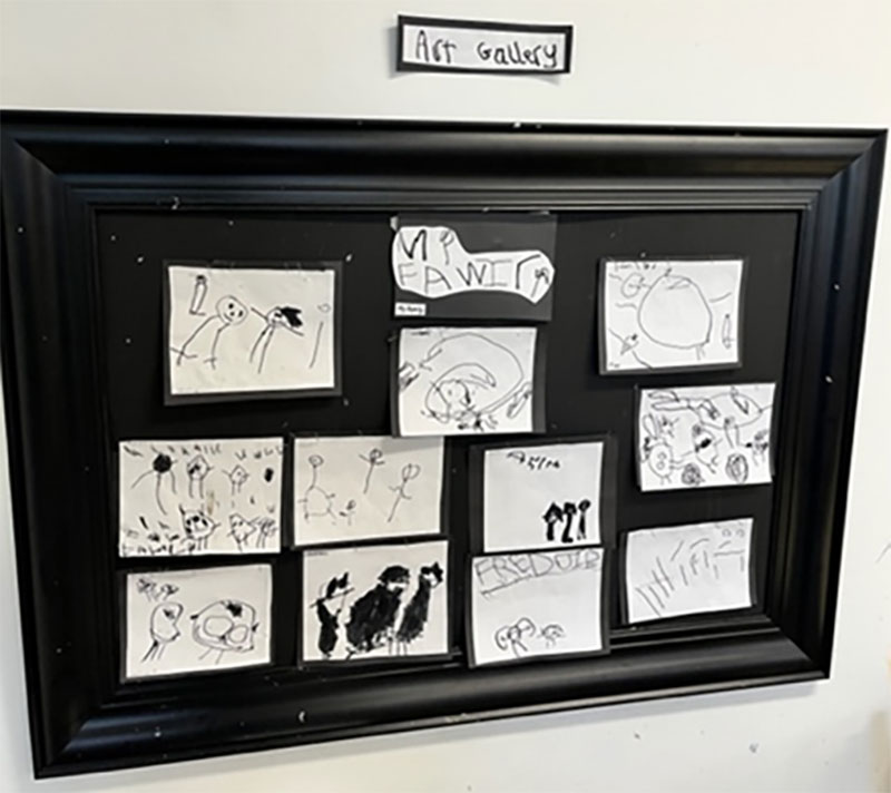 Children's representations of their family on display with art gallery sign above display.