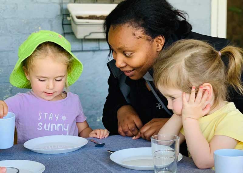 An Educator sits between two children at meal time. In the Circle of Security model, mealtimes provide Educators with the opportunity for interactions that help develop bonds and relationships.