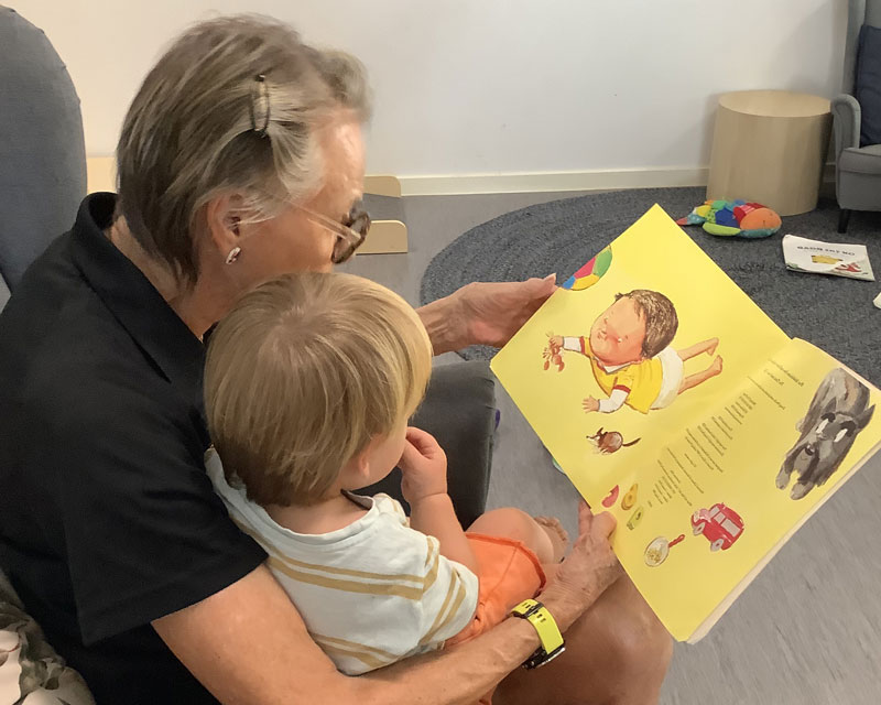 Educator working with multi-aged children reads a book to a child.