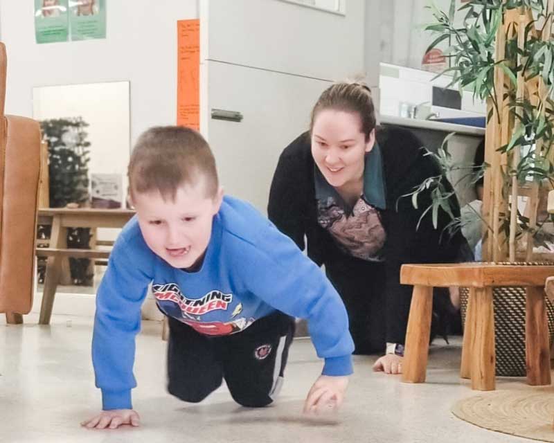 An educator gets down to a child's level to crawl across behind them in the environment while teaching them how to Get Down Low & GO, GO. Role modelling is one teaching method to develop learning dispositions in early childhood.