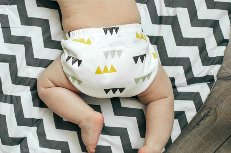 A child lies on its bellow on mat while wearing patterned cloth nappies for newborns.