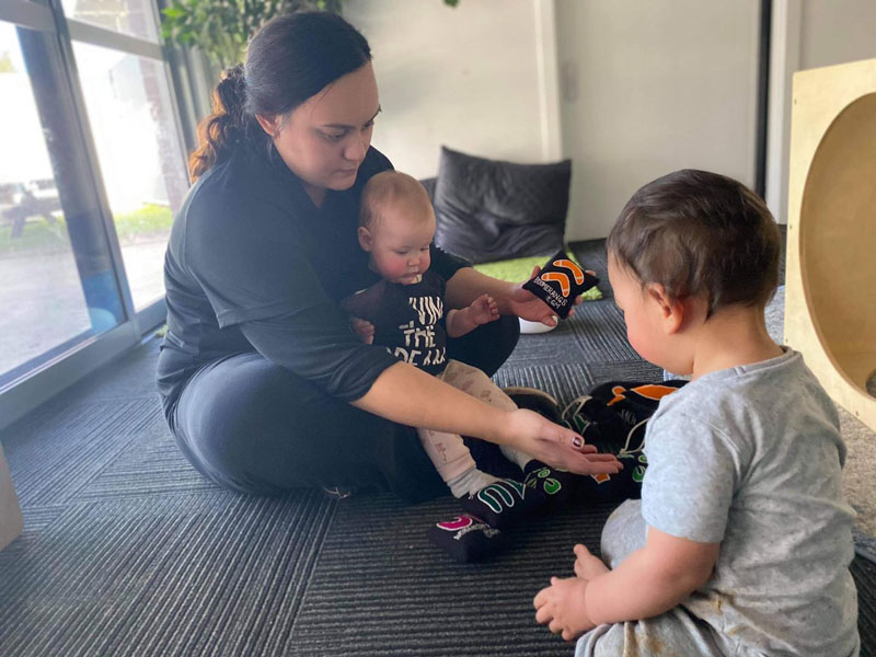 An educator sits on the floor holding one child in their lap and playing with with another while using the circle of security as a road map to respond to both their social needs.