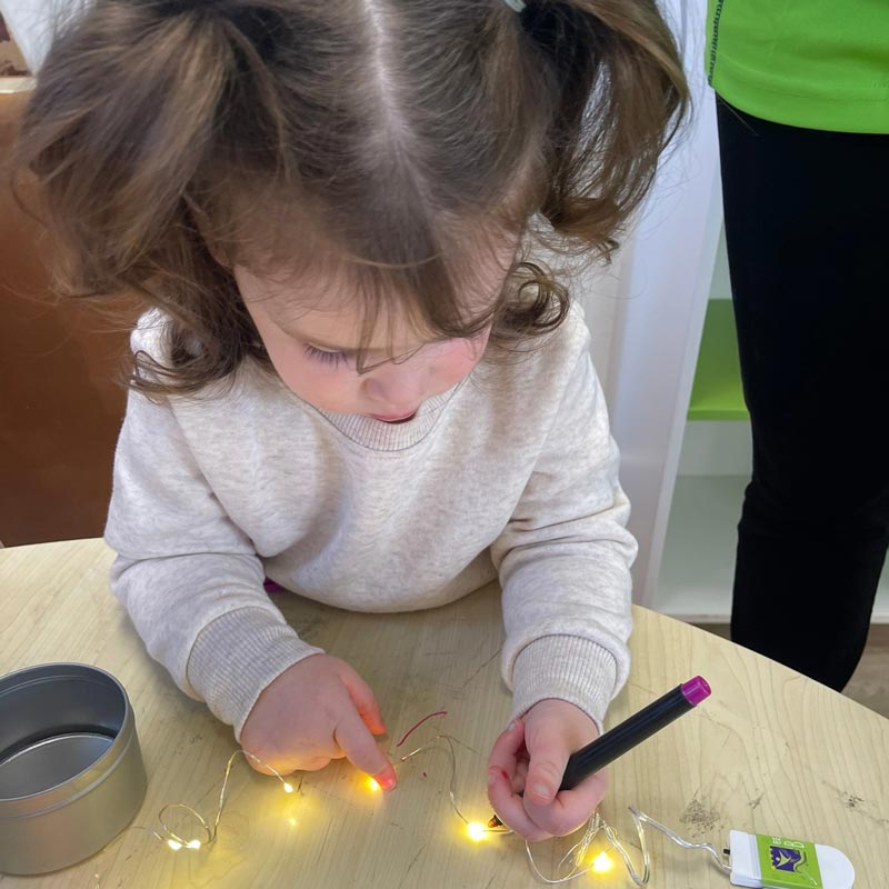 Child holds pen and fairy lights on a circuit as part of STEM education in early childhood.