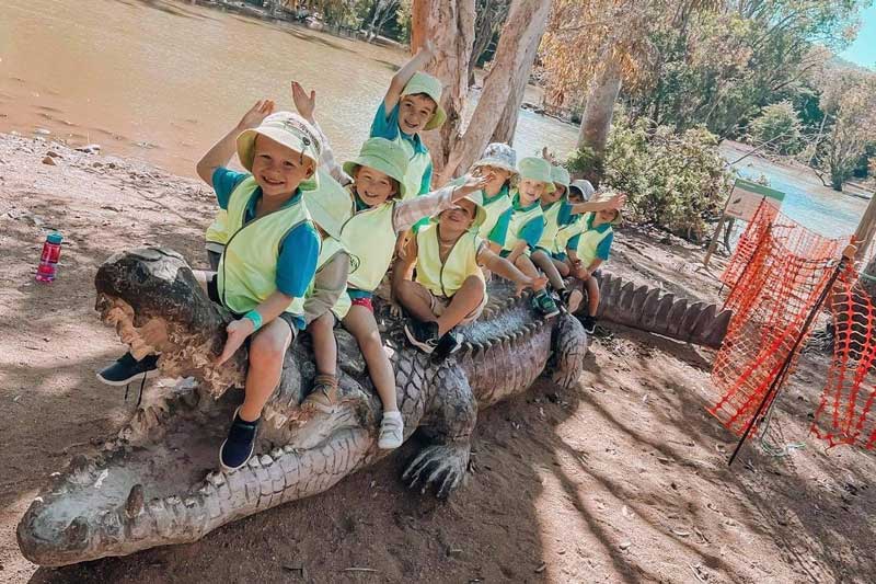 Children sitting on a pretend crocodile, learn the importance of caring for animals at excursions., 