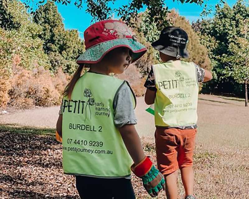 Two children in parkland with Petit ELJ yellow vests on participate in Bush Kindy making learning visible in their community.