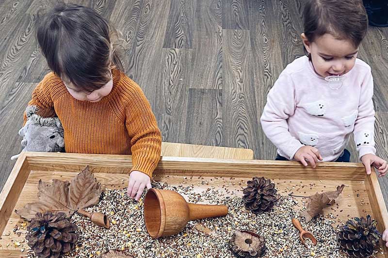 Two children stand behind a loose-parts table filled with natural materials that encourage children to learn about nature and sustainability.