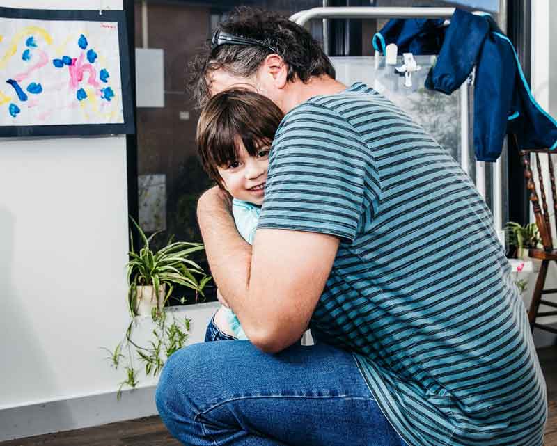 Dad hugs child in front of their child care art exhibition. One of many fun Father's Day activities.