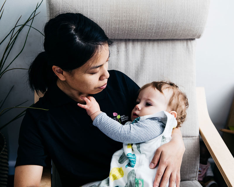 An educator sits in a chair holding a baby and making connections. Making you and baby comfortable may require repurposing the family room in a small house with a baby.