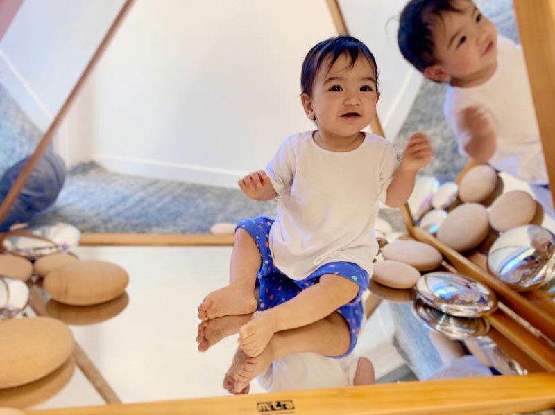 Young child sits on mirror learning aid with wooden and shiny circles. Child's reflection and photography tools for creating a strong sense of identity.