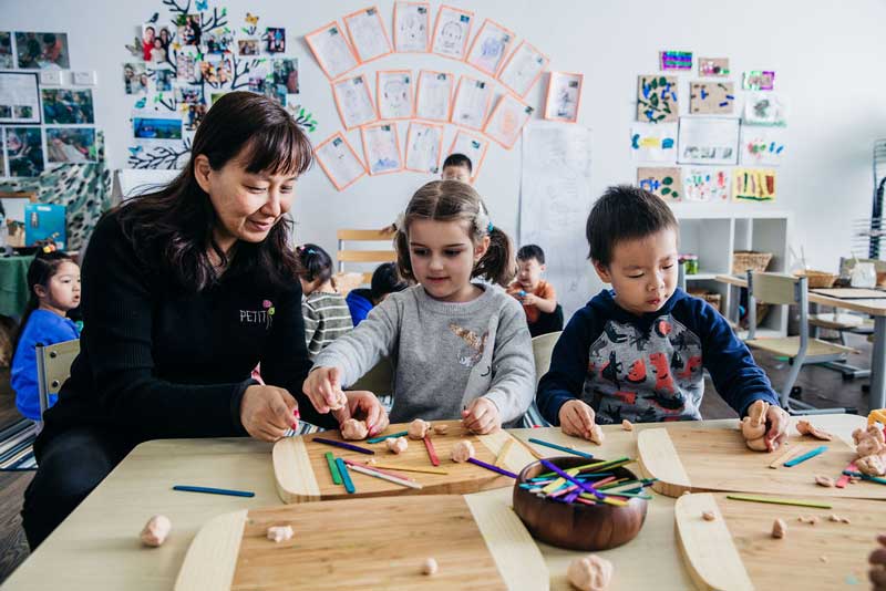 An Educator and two children use playdough and pop sticks for a play-based learning experience.