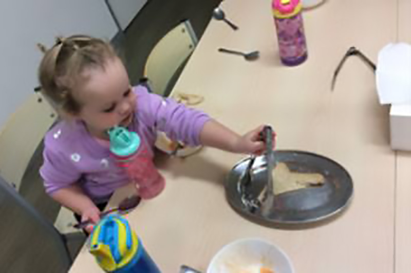 Child sits around lunch table learning about self-serving or serve and return, which reflects loose parts theory. 