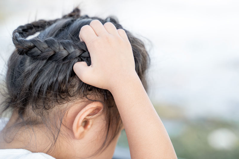 Child scratching head, could be a sign of lice and nits in hair.