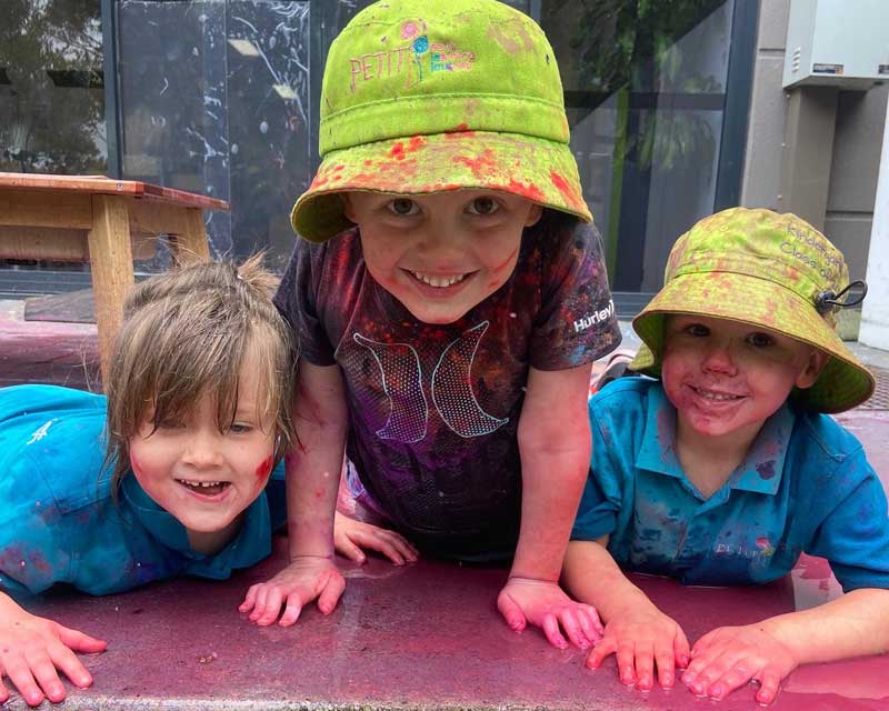 Three children pose for a photo covered in coloured flour while celebrating Holi and developing a sense of identity and a sense of community.