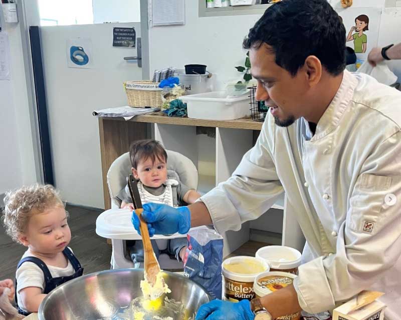 Chef Terrance inspires the next generation of chefs with his children's cooking experience. Children look on as he mixes in a big silver bowl.