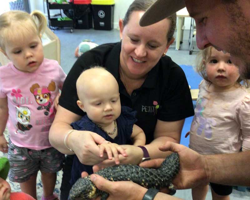  Being an educator: Amy helps a young child pet a lizard and develop an appreciation for animals while two other children watch on.