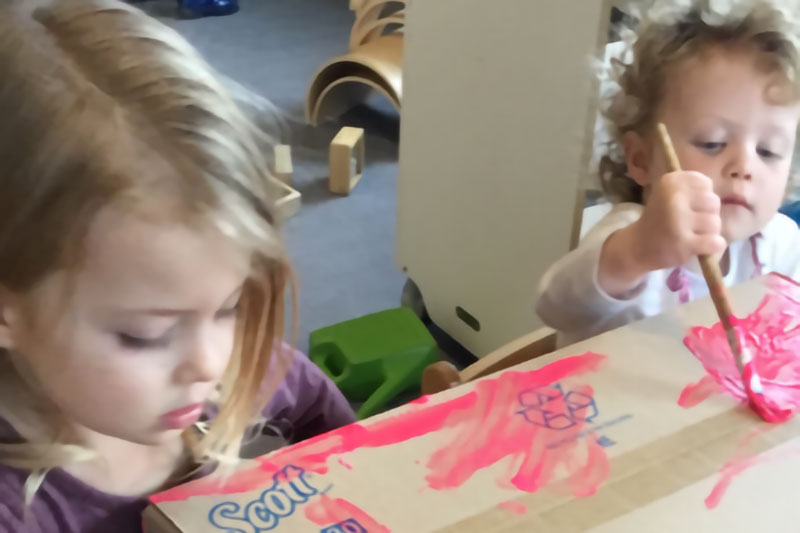 Close-up of a baby and preschooler decorating a child's keepsake box.