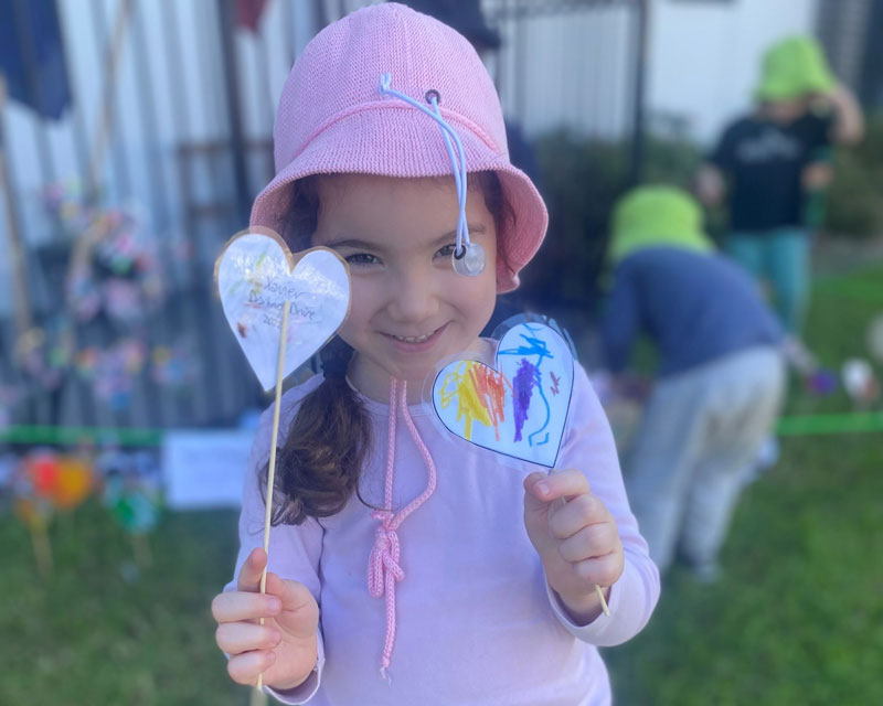 Child holds two Sea of Hearts to engage with reconciliation while in background children create a display with many Hearts made by children and families..