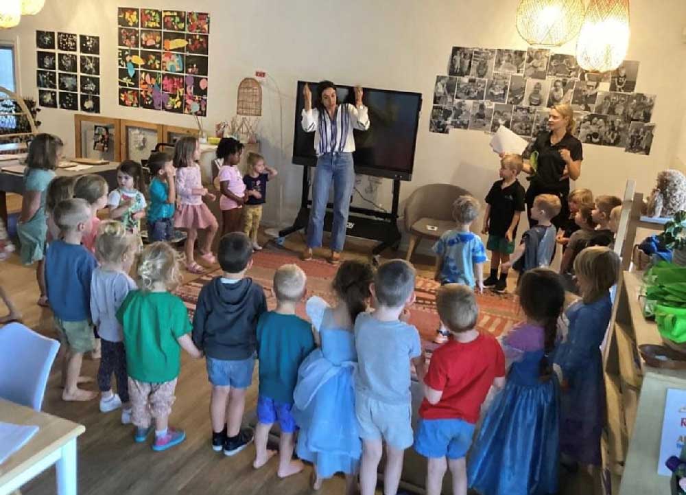 Behind ths group of children who are taking spanish lessons, educators have made learning visible in the studios through photos and art placed on the walls where families can see it.