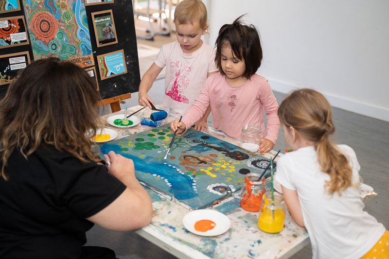  An educator observes and interacts with three children as they work together in a group to create a painting. Educators are always learning from children in ECEC where there are different career pathways. 