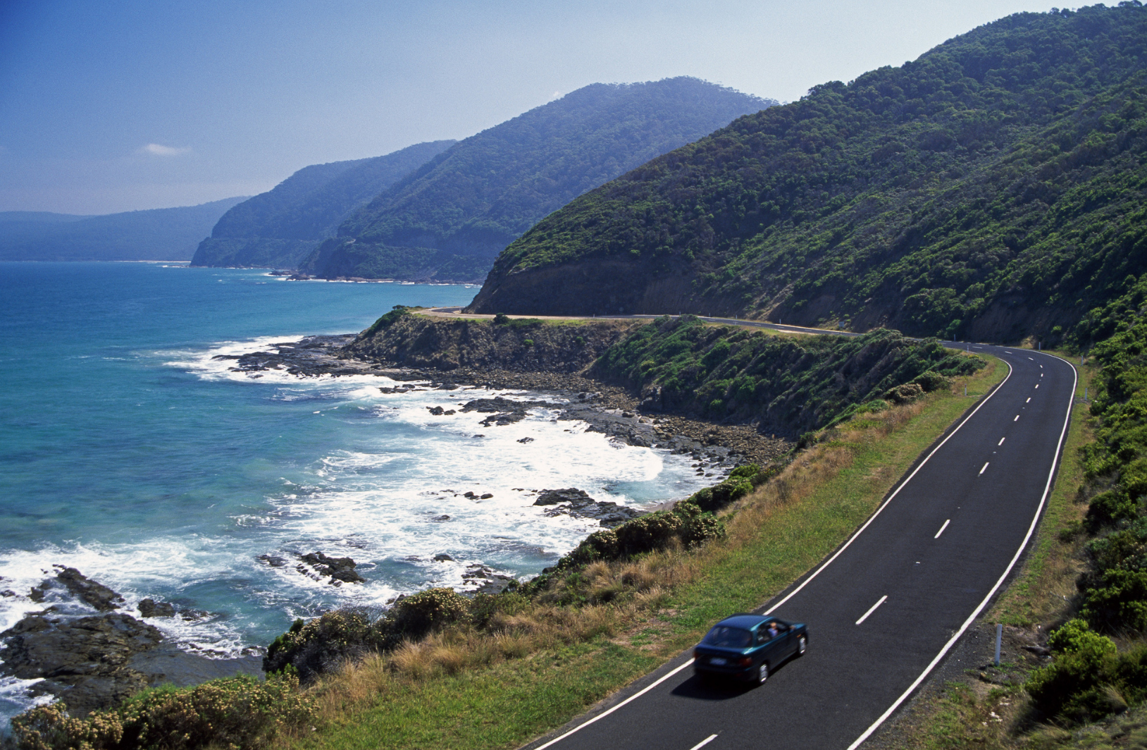 Car travelling along the Great Ocean Road in Victoria, Australia with mountains ahead.