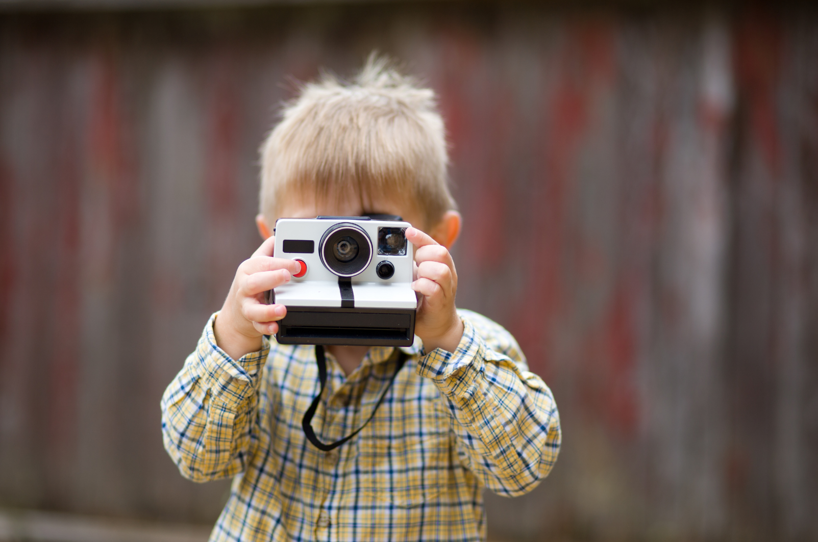 Young boy child holding up a polaroid instant camera to his face looking through the lens ready for holiday travelling